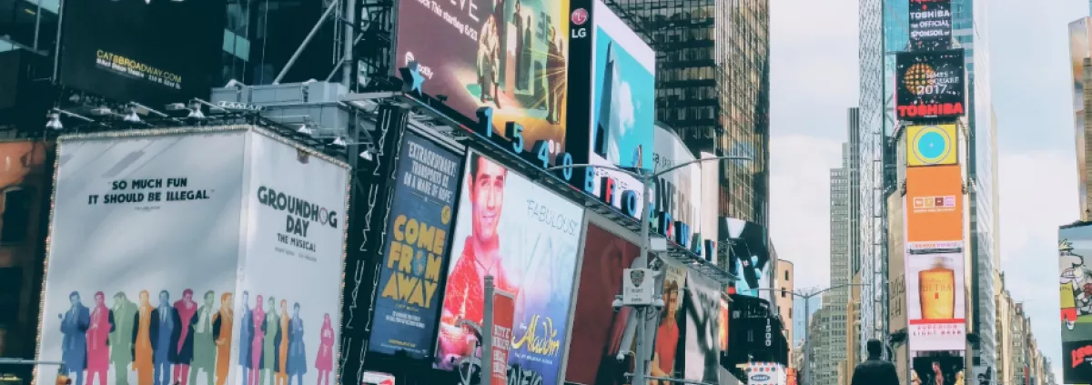 Une photo d'une grande rue avec des hauts immeubles et beaucoup d'affiches publicitaires accrochée dessus.